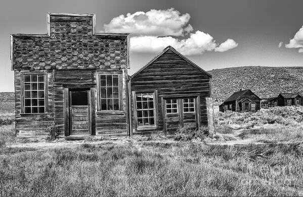 Black & White;black + White;monochrome;black And White;architecture;detail;details;cabins;structures;wood;windows;doors;door;window;buildings;dilapidated;rundown;abandoned;forlorn;derelict;empty;sandra Bronstein;clouds;doorways;entrances;old West;out West;bodie;ghost Town;ghost Towns;california;gold Rush Days;mining;houses;house;residence;horizontal;fine Art Photography;iconic;travel;tourism;historical;state Park;popular;dated;unoccupied;panes;glass;western United States;canvas; Poster featuring the photograph Days of Glory Gone by Sandra Bronstein