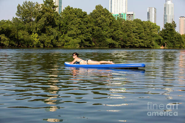 Woman Poster featuring the photograph A female stand up paddle board lounges on the crystal clear blue waters of on Lady Bird Lake in Austin, Texas- Stock Image by Dan Herron