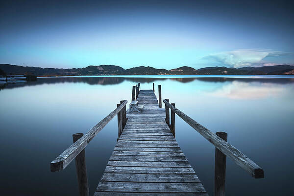 Lake Poster featuring the photograph Wooden pier or jetty on a blue lake sunset and sky reflection on #1 by Stefano Orazzini