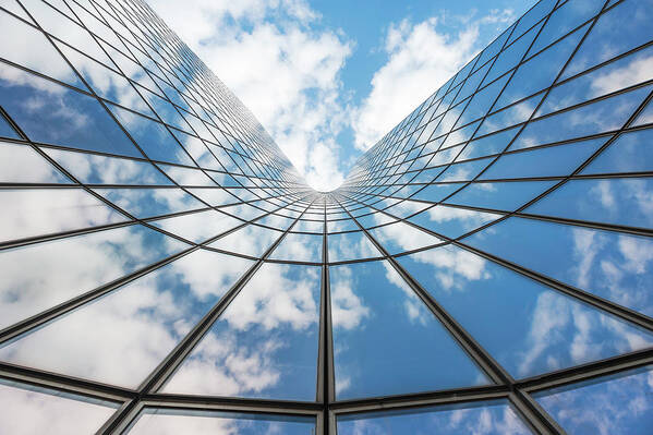 Building Poster featuring the photograph Blue sky and white clouds reflecting in a glass building by Philippe Lejeanvre