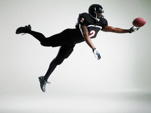 American Football Uniform Poster featuring the photograph Football Player Leaping In Mid Air To by Thomas Barwick