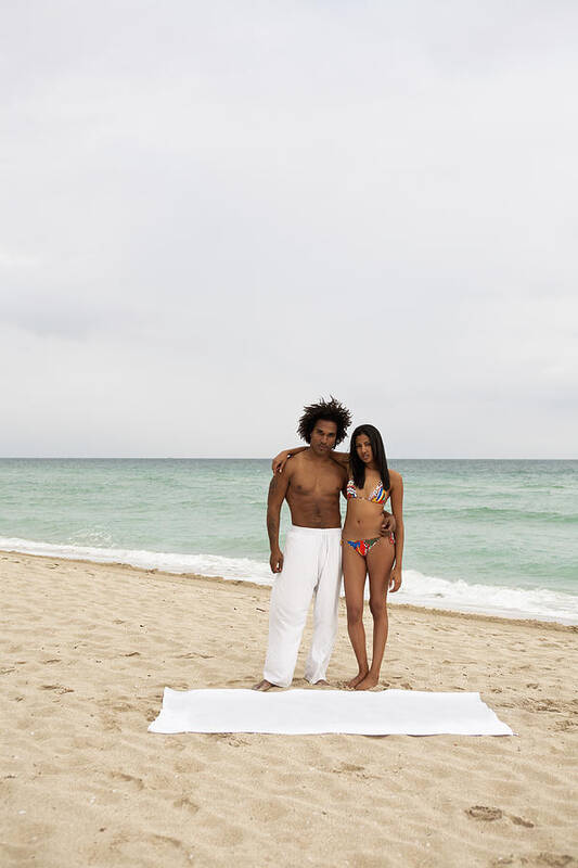 Young Men Art Print featuring the photograph An attractive young couple standing on a beach by Emiliano Granado