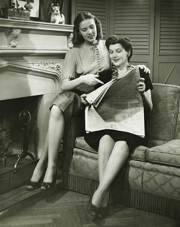 Mature Adult Art Print featuring the photograph Two women sitting by fireplace, reading newspaper, (B&W) by George Marks