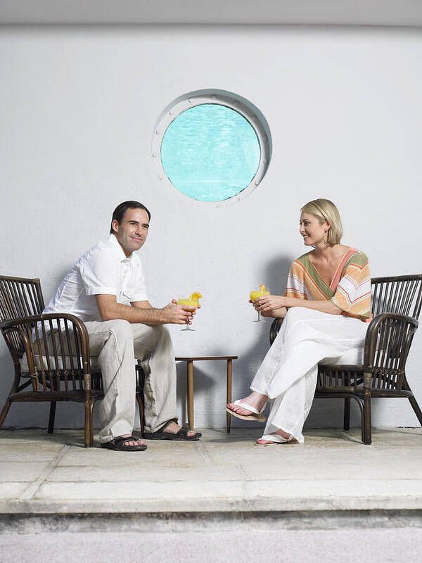 Part Of A Series Art Print featuring the photograph Couple Sit Holding Cocktails on a Pavement in Front of a Wall With a Port-Hole by Digital Vision.
