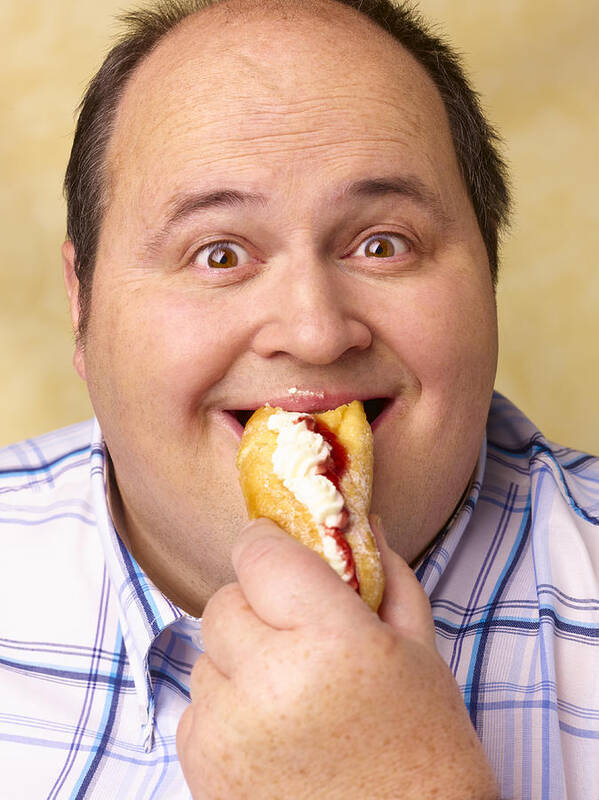 Holding Art Print featuring the photograph Obese man eating cream cake. by Peter Dazeley