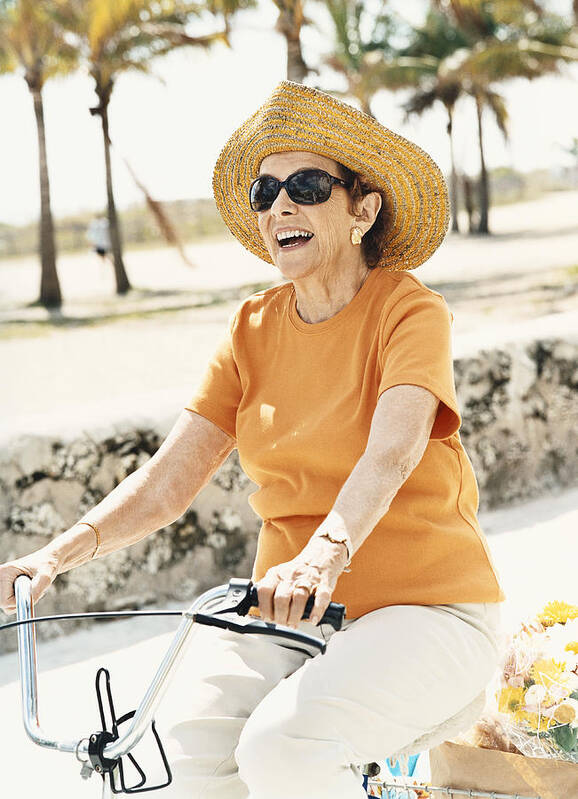 Non-urban Scene Art Print featuring the photograph Senior Woman Wearing a Sun Hat and Riding a Bicycle by Digital Vision.