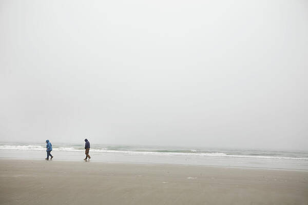 Beach Art Print featuring the photograph A Couple Walks On The Shore Of A Foggy by Eyeconic Images