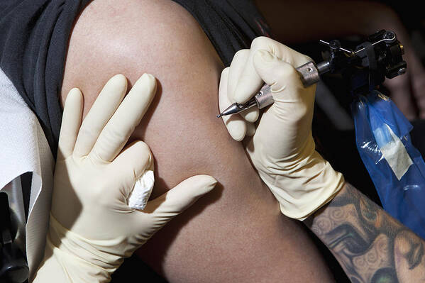 Expertise Art Print featuring the photograph A tattoo artist preparing to tattoo a man's bare arm, close-up by Halfdark