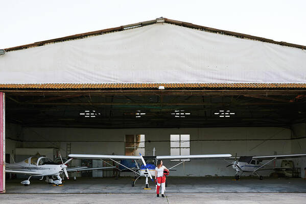 Skydivers Art Print featuring the photograph Young Female Skydiver In A Plane Hangar Surrounded By Planes #1 by Cavan Images