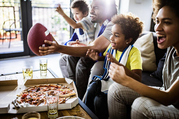 Unhealthy Eating Art Print featuring the photograph Cheerful black family cheering while watching rugby match on TV at home. by Skynesher