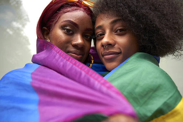 Youth Culture Art Print featuring the photograph Two women wrapped in Pride Flag #1 by We Are