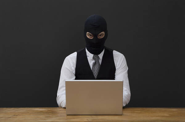 Balaclava Art Print featuring the photograph A man wearing a balaclava and using a laptop by Andreas Schlegel