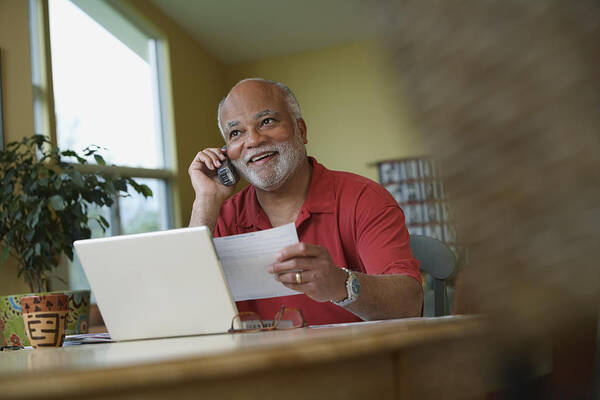 Debt Art Print featuring the photograph African man talking on telephone while paying bills by Jon Feingersh Photography Inc