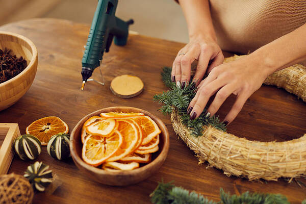 People Art Print featuring the photograph Close-up of unrecognizable woman with manicure standing at wooden table in workshop and using hot glue while attaching fir tree twigs to wreath base by Mediaphotos