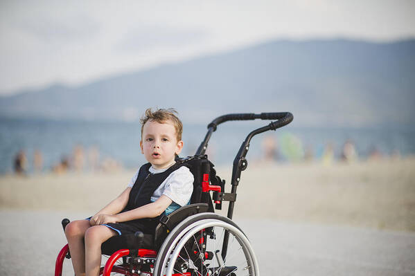 Water's Edge Art Print featuring the photograph Cute young boy on the wheelchair by the sea by Dmphoto