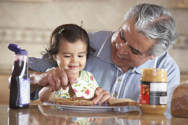 Care Art Print featuring the photograph Grandfather helping granddaughter (12-15 months) make sandwich by SW Productions