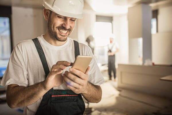Expertise Art Print featuring the photograph Happy construction worker using cell phone during home renovation. by Skynesher