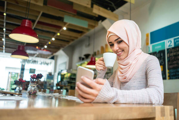 Internet Art Print featuring the photograph Muslim woman at a cafe texting on her mobile phone by Andresr