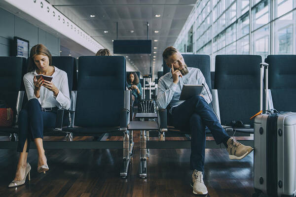Mid Adult Men Art Print featuring the photograph Thoughtful businessman looking away while sitting by female colleague at waiting area in airport by Maskot