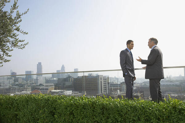 Young Men Art Print featuring the photograph Two businessmen on rooftop talking, side view by Justin Pumfrey