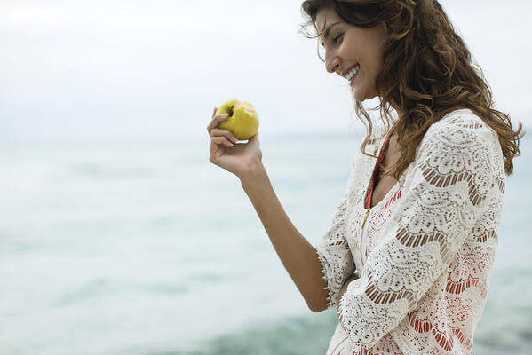 Water's Edge Art Print featuring the photograph Woman eating apple at the beach by PhotoAlto/Antoine Arraou