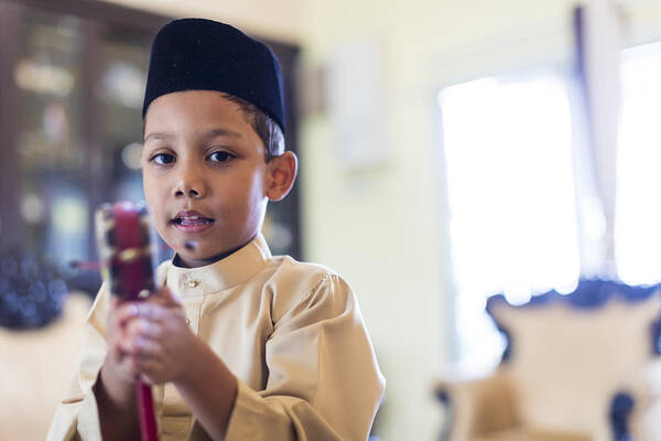 Islam Art Print featuring the photograph Young Malaysian boy in traditional clothing playing with his toy . by GCShutter