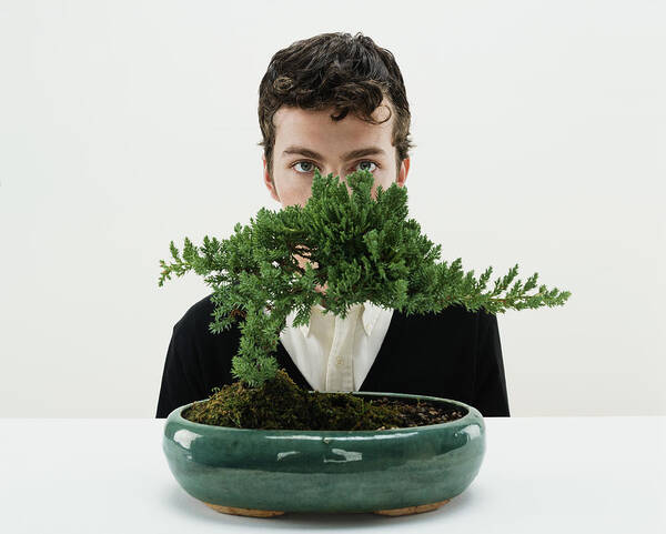 White Background Art Print featuring the photograph Young man behind bonsai tree, portrait by Digital Vision