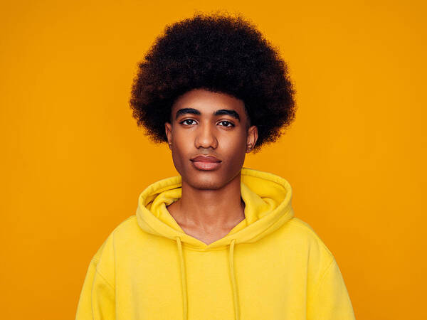 Young Men Art Print featuring the photograph African american man with afro hair wearing hoodie and standing over isolated yellow background by CoffeeAndMilk