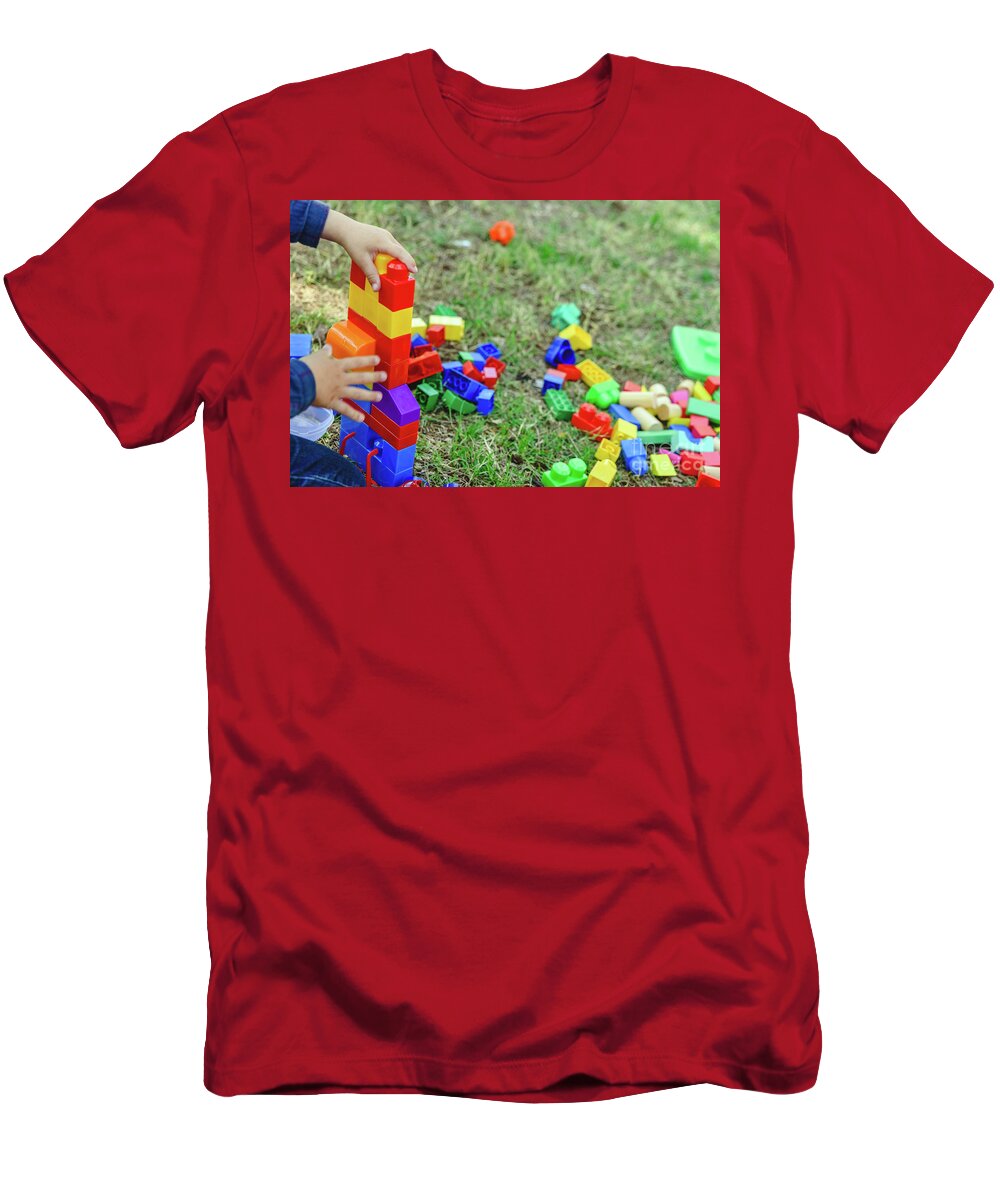 Activity T-Shirt featuring the photograph Child playing with colorful blocks sitting on the ground of a garden in spring, negative space. by Joaquin Corbalan