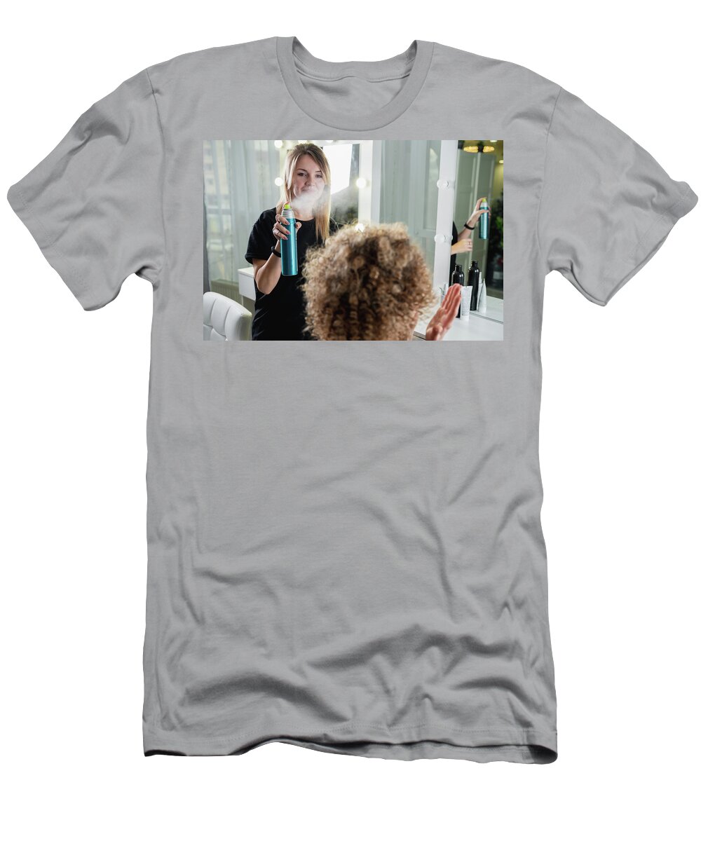 Beauty T-Shirt featuring the photograph Closeup of hairdresser using hairspray on client's hair at salon by Maria Kray
