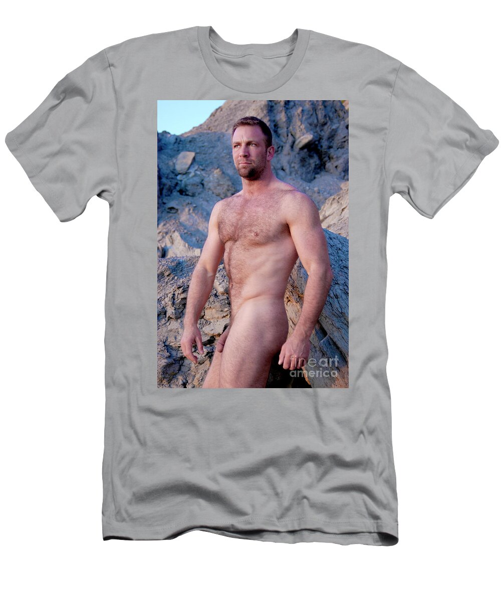 Young T-Shirt featuring the photograph Rugged masculine nude man poses by cliffs my the ocean. by Gunther Allen