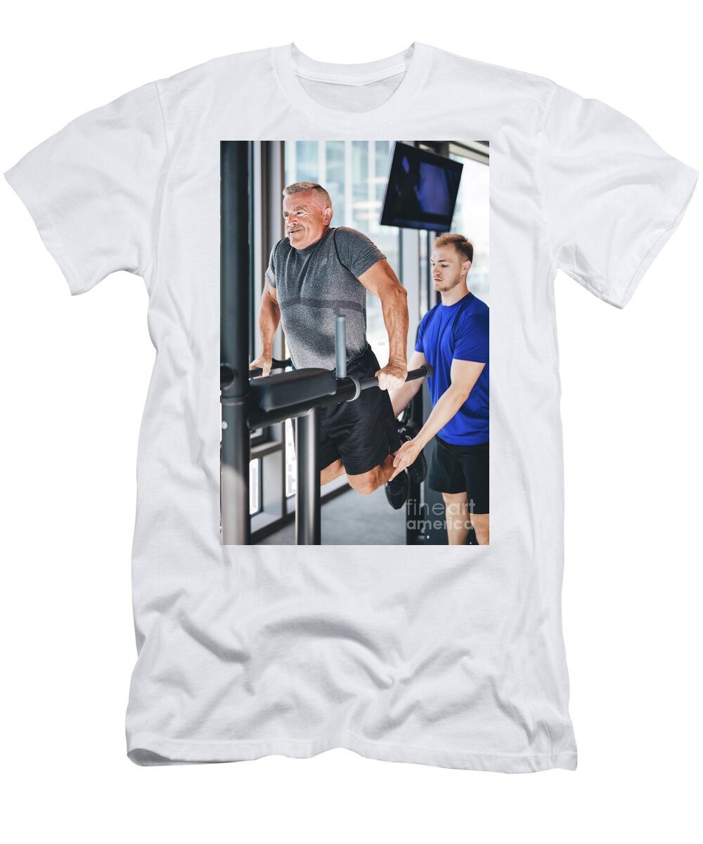 Man T-Shirt featuring the photograph Gym instructor helping senior man at the gym. by Michal Bednarek
