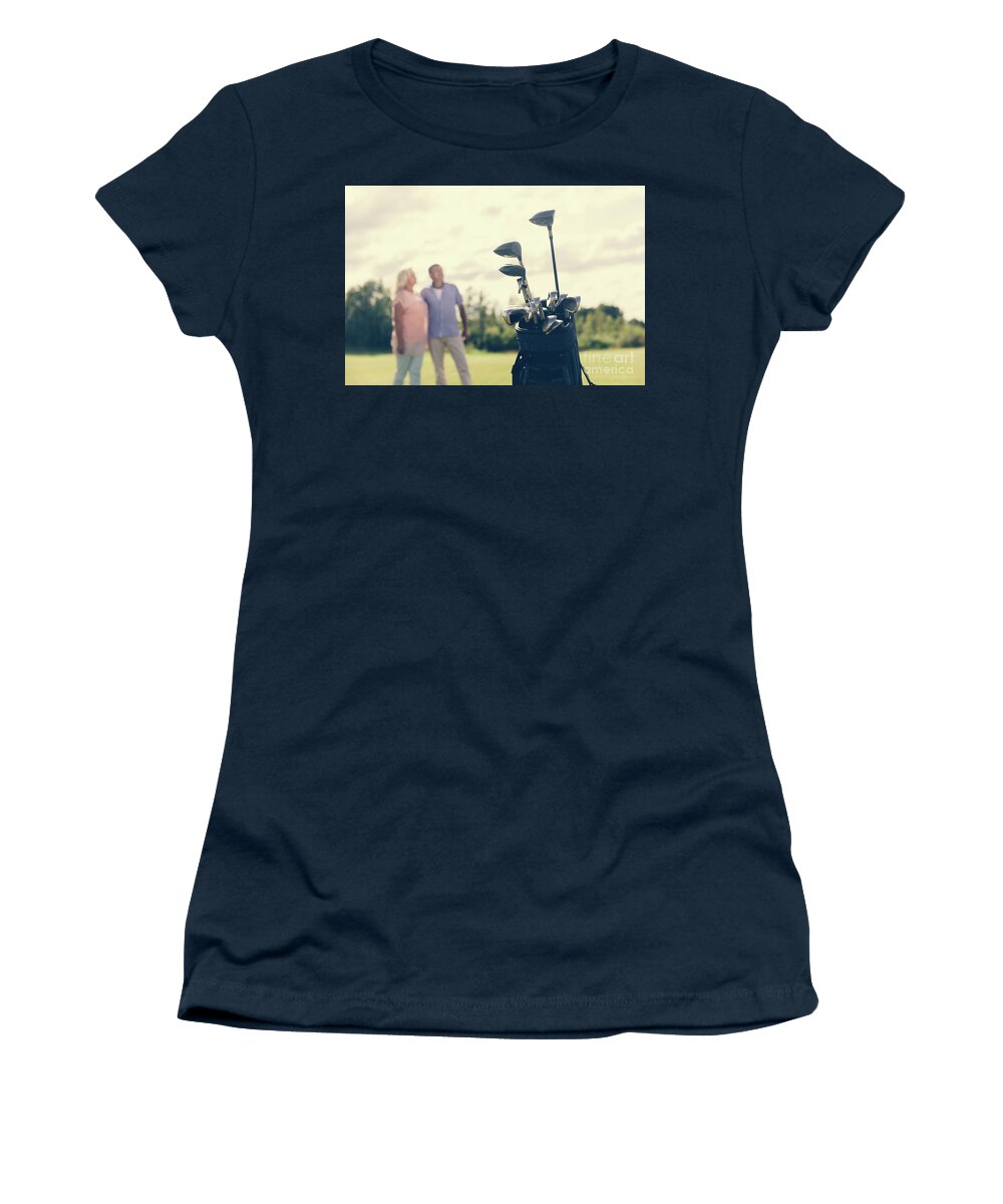 Golf Women's T-Shirt featuring the photograph Golf bag standing on a grass field, people in the background by Michal Bednarek