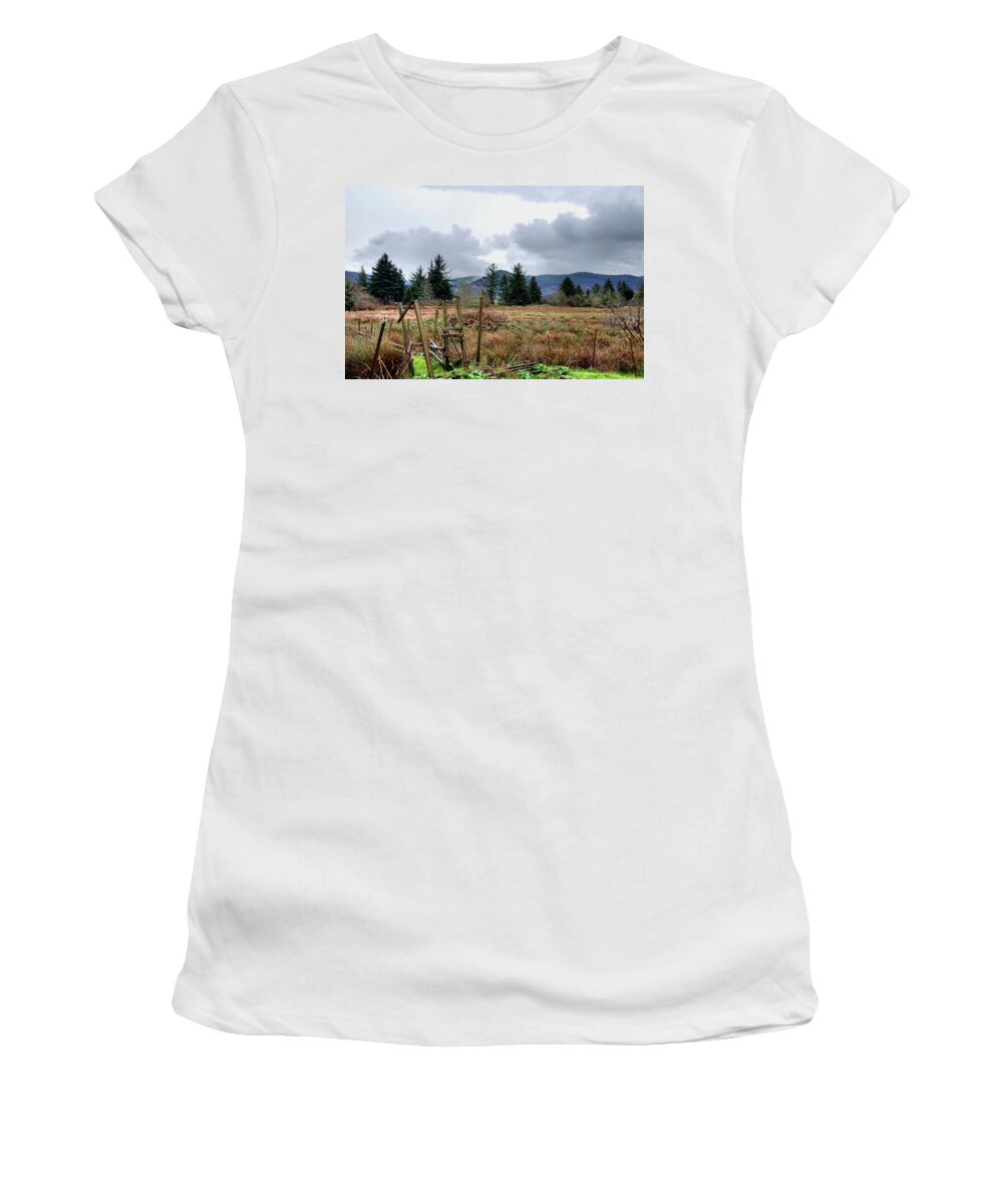 A Slight Mist Or Fog Veils Parts Of Distant Hills Beneath Troubled Skies. Women's T-Shirt featuring the photograph Field, Clouds, Distant Foggy Hills by Chriss Pagani