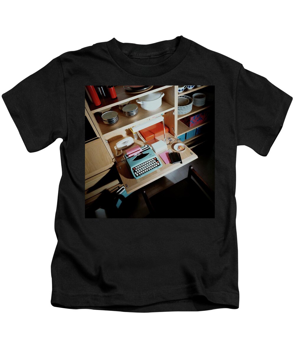Indoors Kids T-Shirt featuring the photograph A Cupboard With A Blue Typewriter by Ernst Beadle