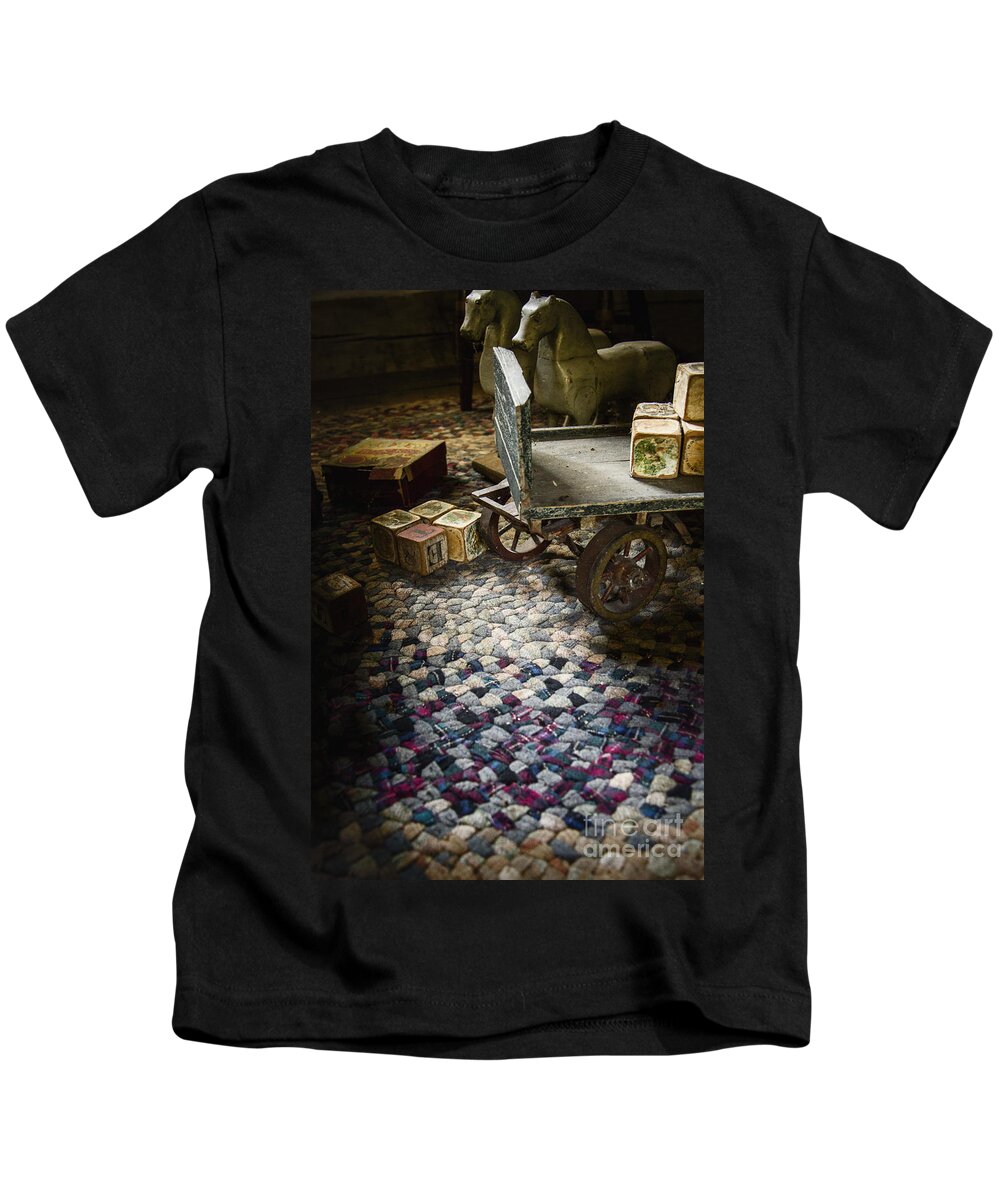 Vintage; Antique; Blocks; Toy; Toys; Child; Children; Child's; Still Life; Rug; Letters; Alphabet; Pictures; Wagon; Horses; Play; Playroom; Worn; Dirty; Shadows; Eerie; Mystery; Mysterious; Shroud; No One; Empty; Floor; Inside; Indoors; Interior Kids T-Shirt featuring the photograph In the Dark Recesses of our Mind by Margie Hurwich