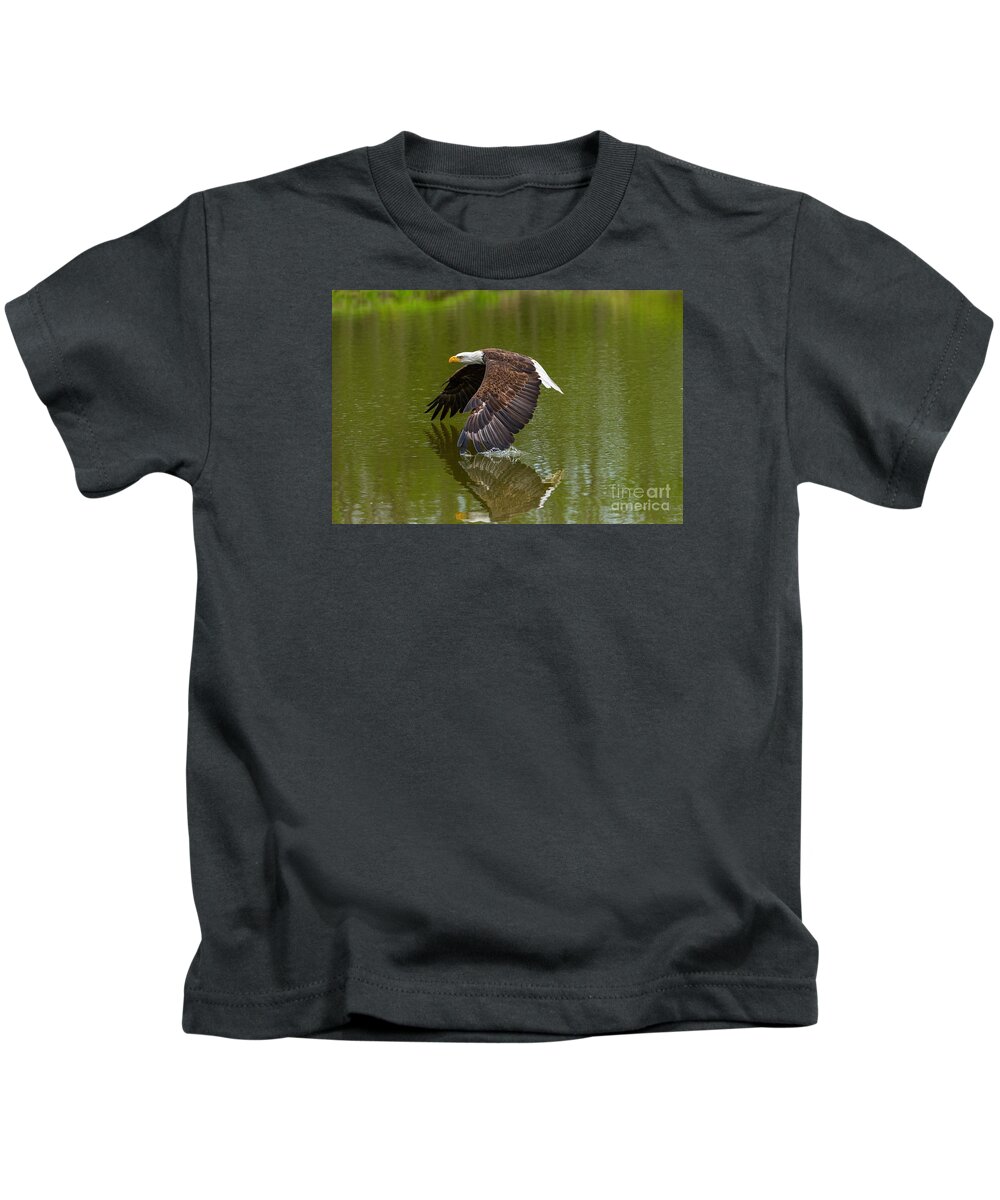 Birds Kids T-Shirt featuring the photograph Bald Eagle in low flight over a lake by Les Palenik