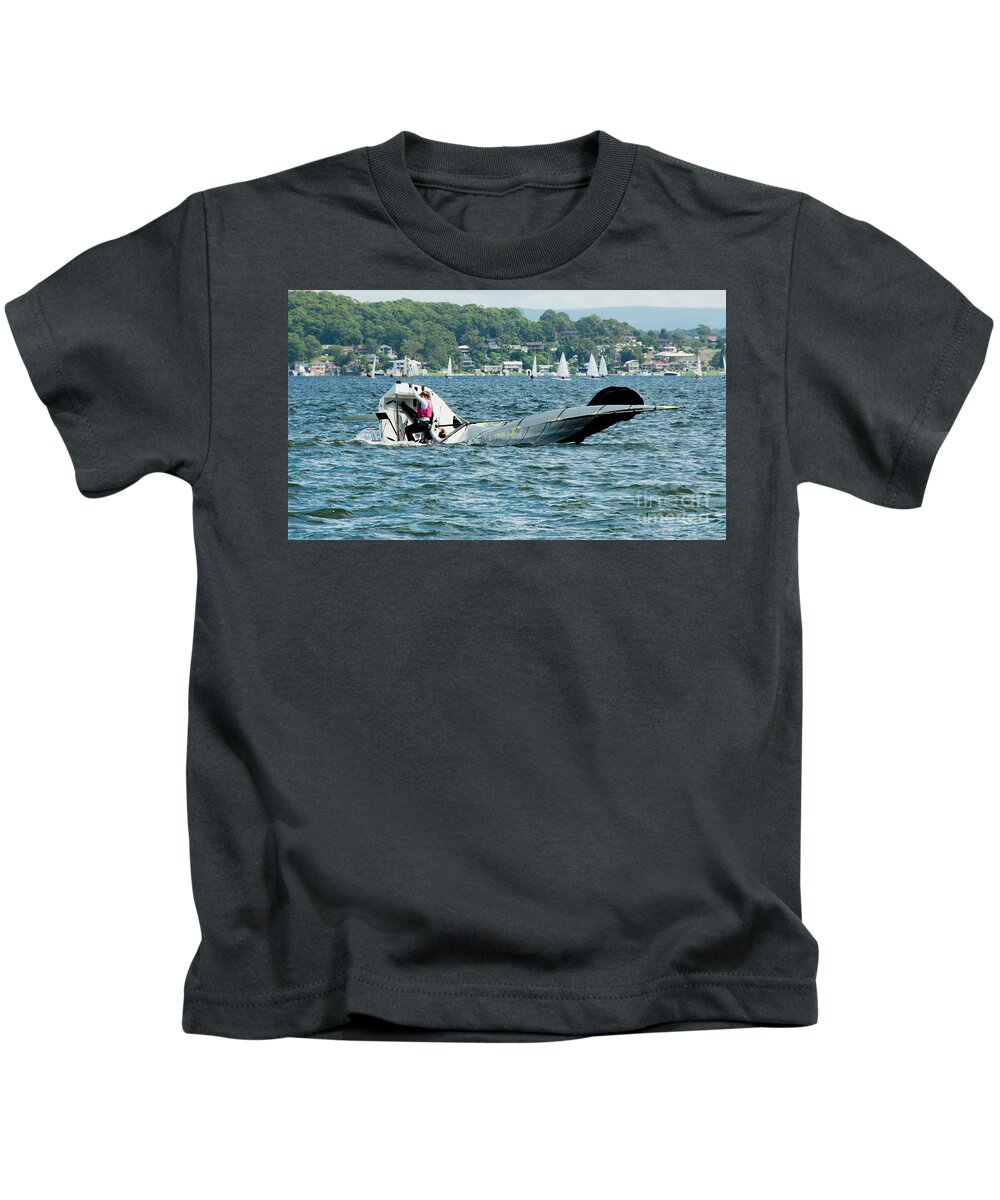 Csne36b Kids T-Shirt featuring the photograph A junior sailor climbing back onboard a capsized sailing skiff. by Geoff Childs