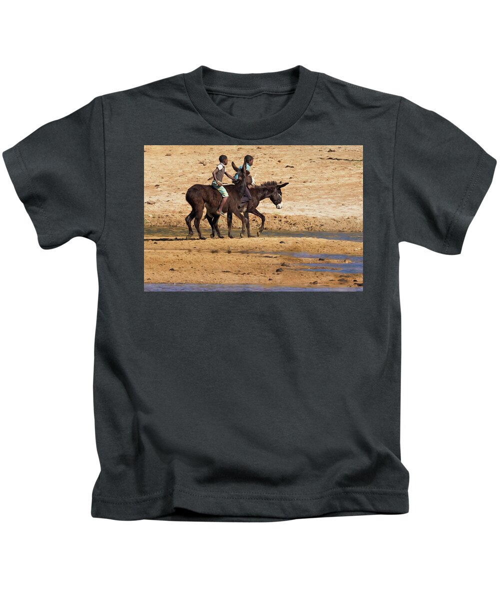 Two Boys Kids T-Shirt featuring the photograph Two Boys Riding Donkeys Along the River in Angola by Belinda Greb