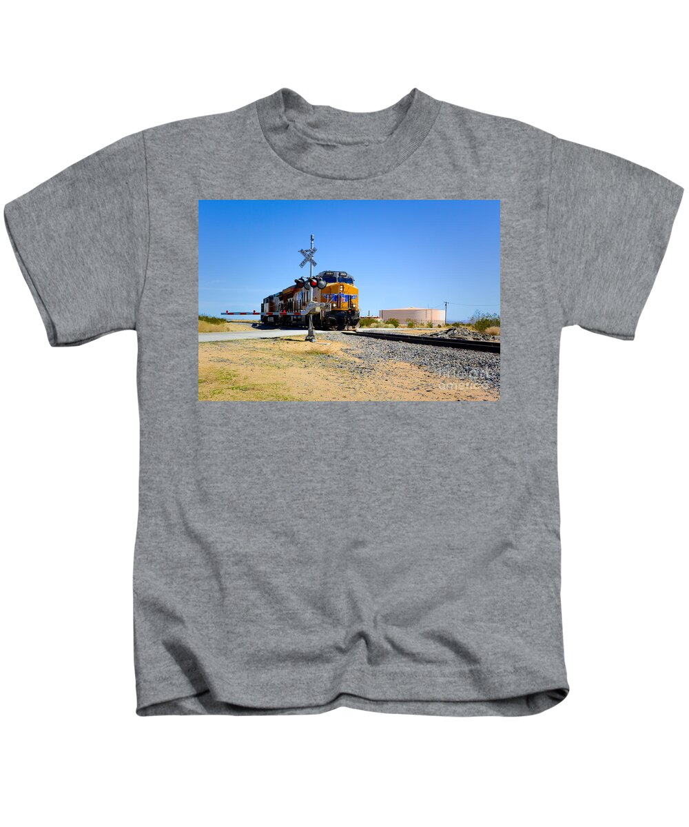 Railway Crossing; Railroad Crossing; Train Crossing; Union Pacific; Freight Train; Yellow; Blue; Green; Red; Water Storage; Train Tracks; Train Signal; Mojave Desert; Mohave Desert; Antelope Valley; Joe Lach Kids T-Shirt featuring the photograph Railway Crossing by Joe Lach