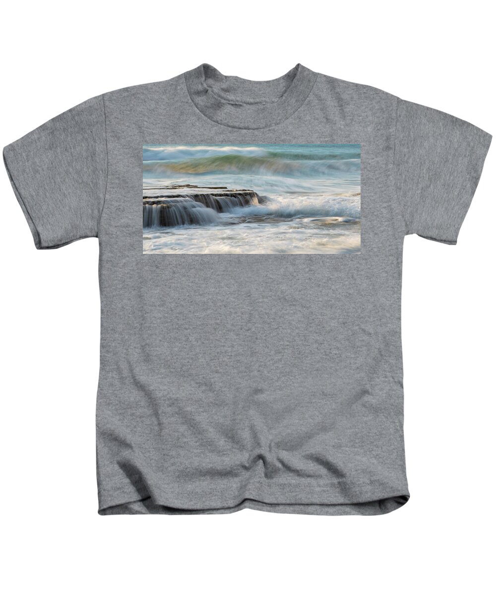 Seascape Kids T-Shirt featuring the photograph Rocky seashore with wavy ocean and waves crashing on the rocks #1 by Michalakis Ppalis