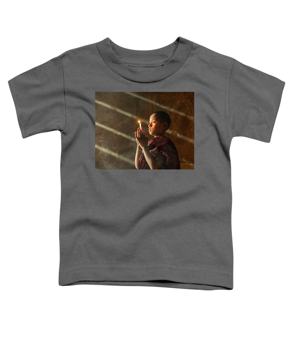 Boy Toddler T-Shirt featuring the photograph A Novice Monk With Candle In Prayer In Temple by Ann Moore