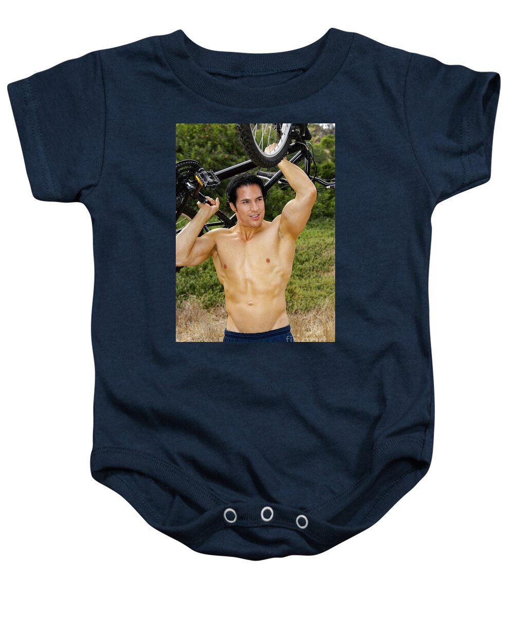 Bicycle Baby Onesie featuring the photograph Hot handsome bicycler lifts his bike above his head. by Gunther Allen