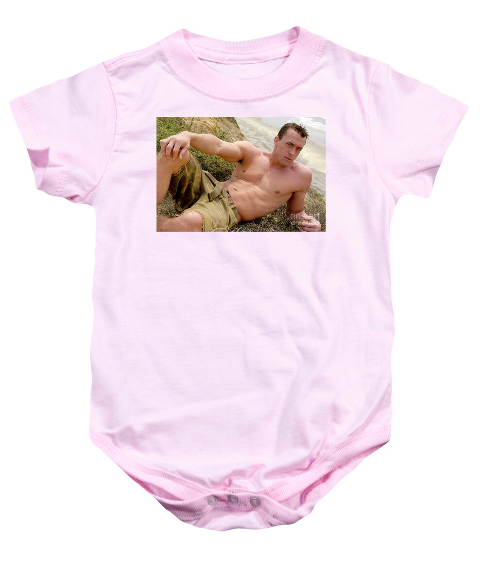 Beach Baby Onesie featuring the photograph Handsome young man poses at the edge of a cliff overlooking the ocean. by Gunther Allen