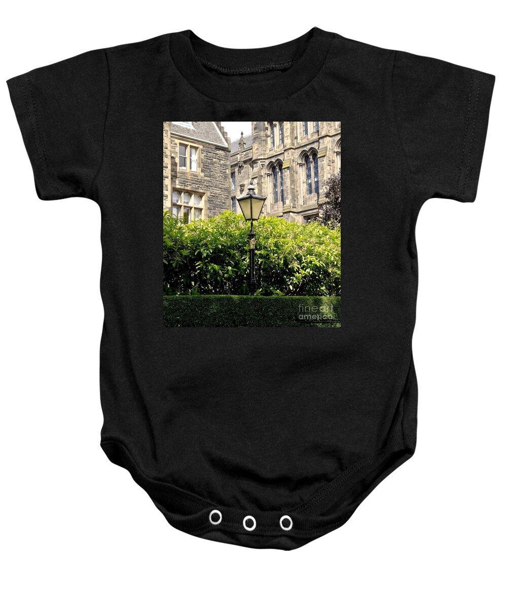 Lamppost Baby Onesie featuring the photograph Lamppost in front of green bushes and old walls. by Elena Perelman