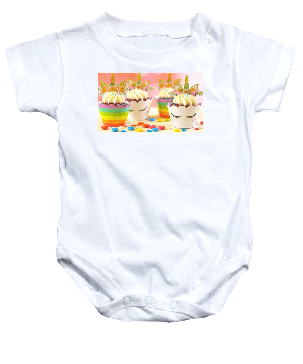 Cupcake Baby Onesie featuring the photograph Decorating children's birthday party unicorn themed cupcakes, closeup. by Milleflore Images