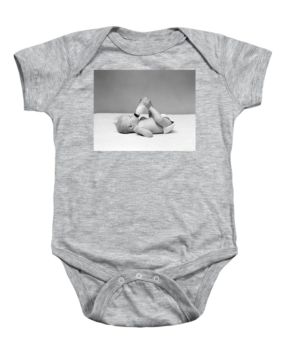 1950s Baby Onesie featuring the photograph Baby Holding Milk Bottle With Feet by H. Armstrong Roberts/ClassicStock