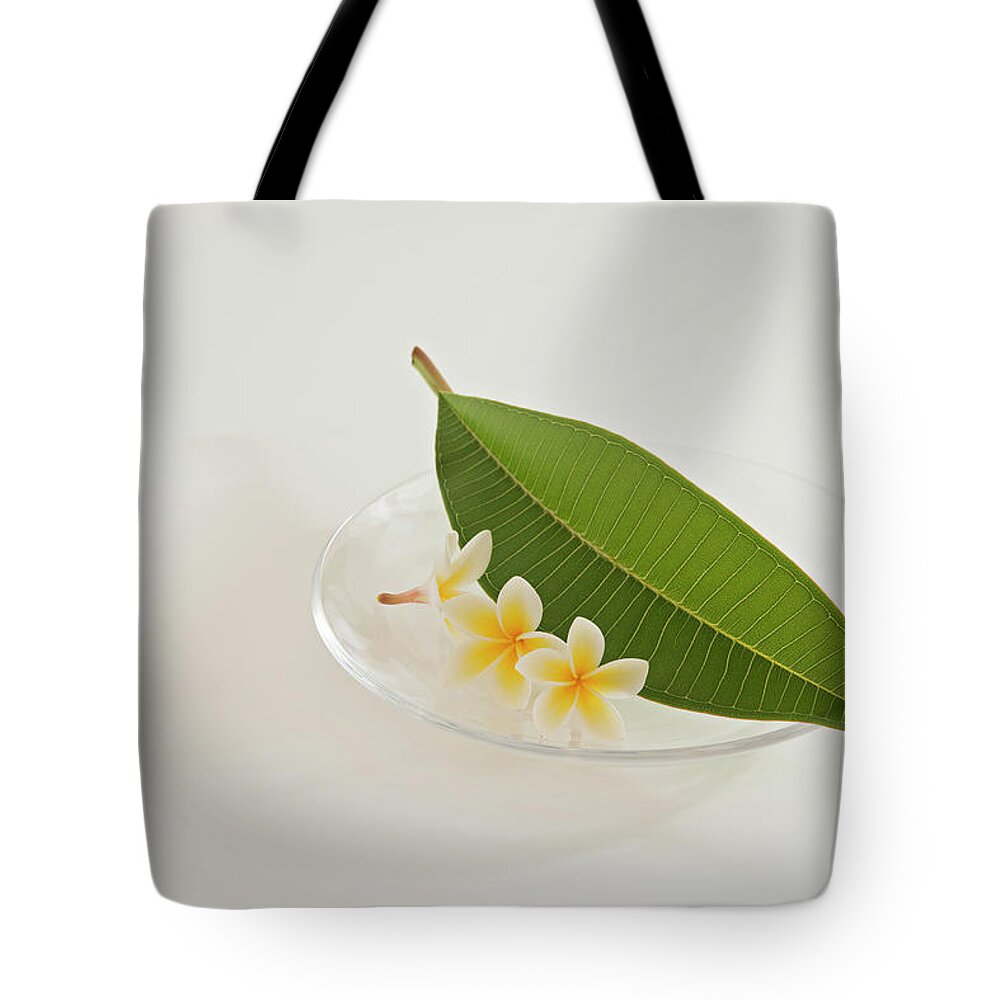 White Background Tote Bag featuring the photograph A Plate Of Plumeria Flowers And Leaf by Margarita Komine
