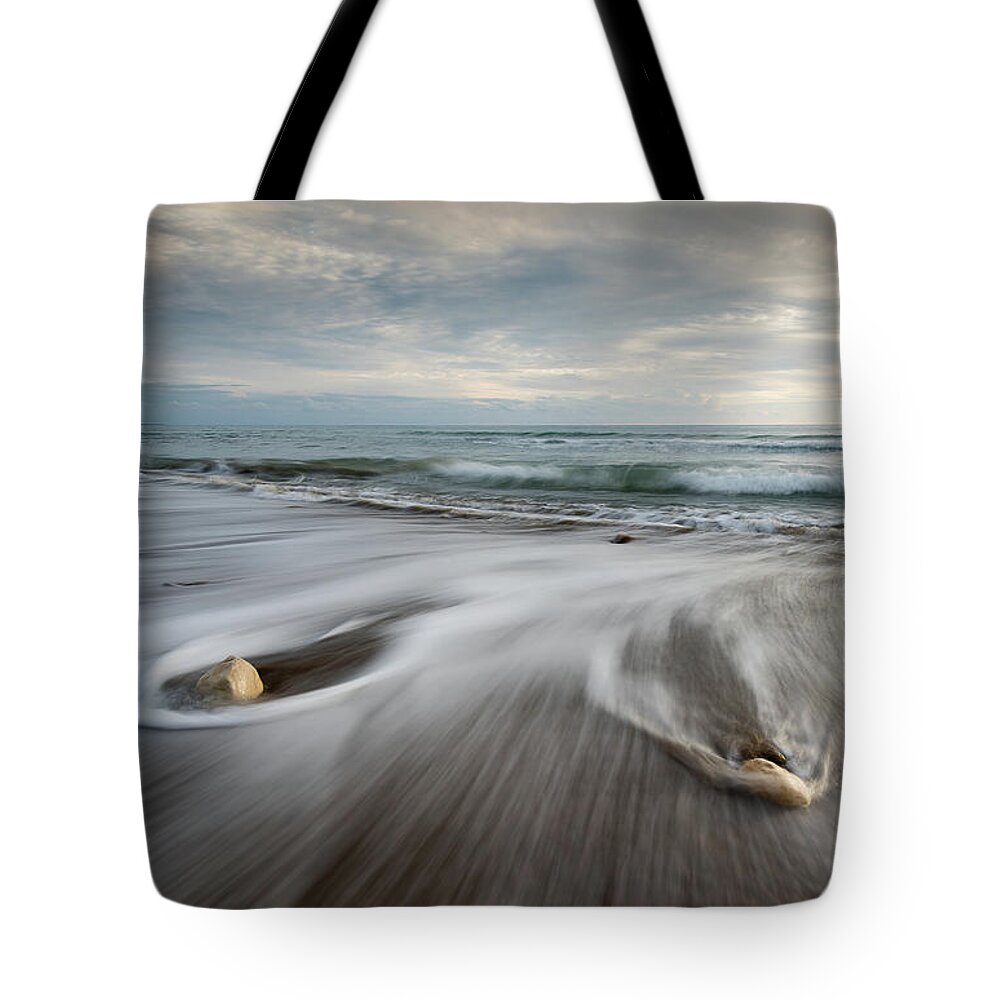 Coastline Tote Bag featuring the photograph Pebbles in the beach and flowing sea water #3 by Michalakis Ppalis