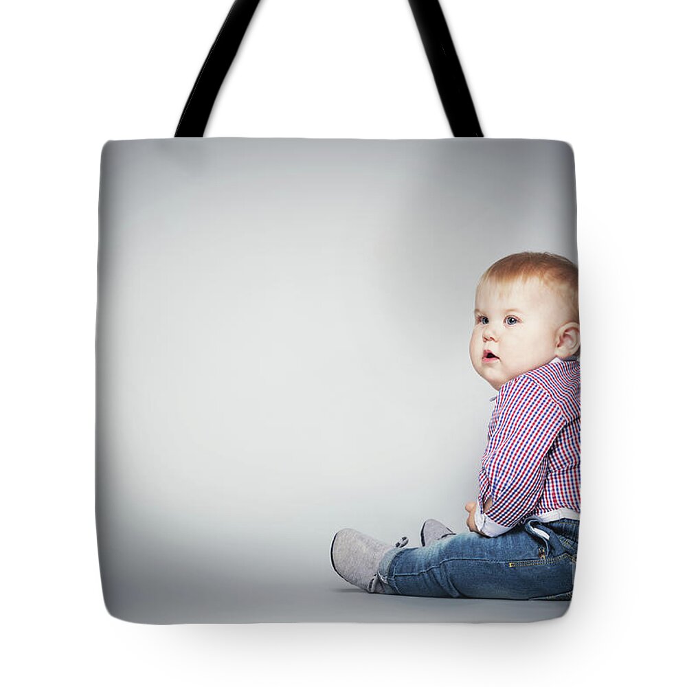 Baby Tote Bag featuring the photograph Cute toddler sitting on the floor. by Michal Bednarek